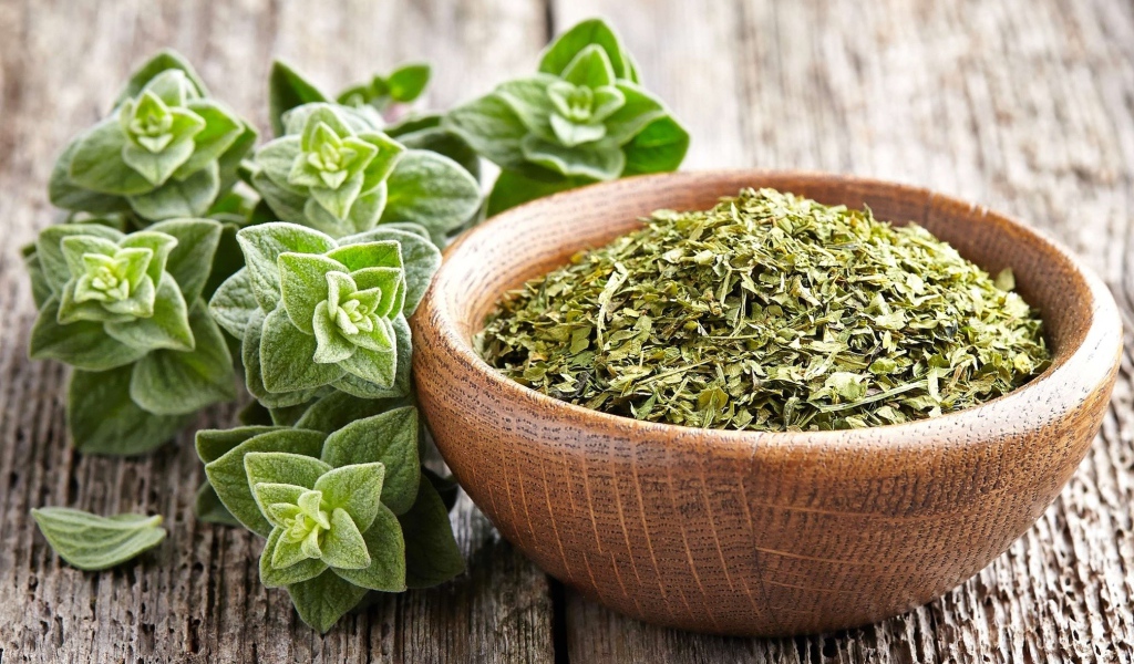 Сухая трава орегано в деревянной миске на столе 