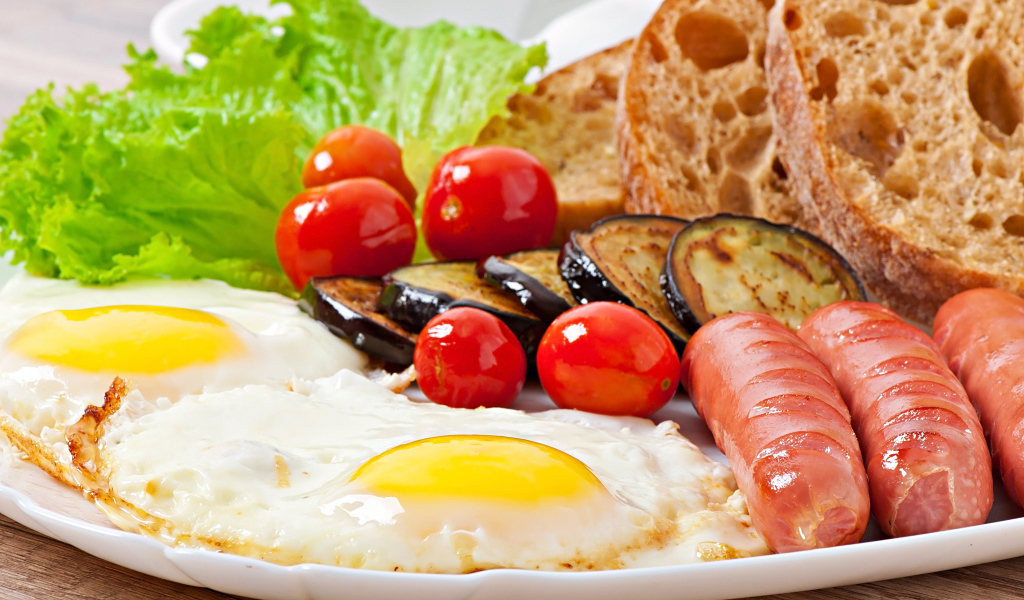 Яичница на тарелке с сосисками, овощами и хлебом
