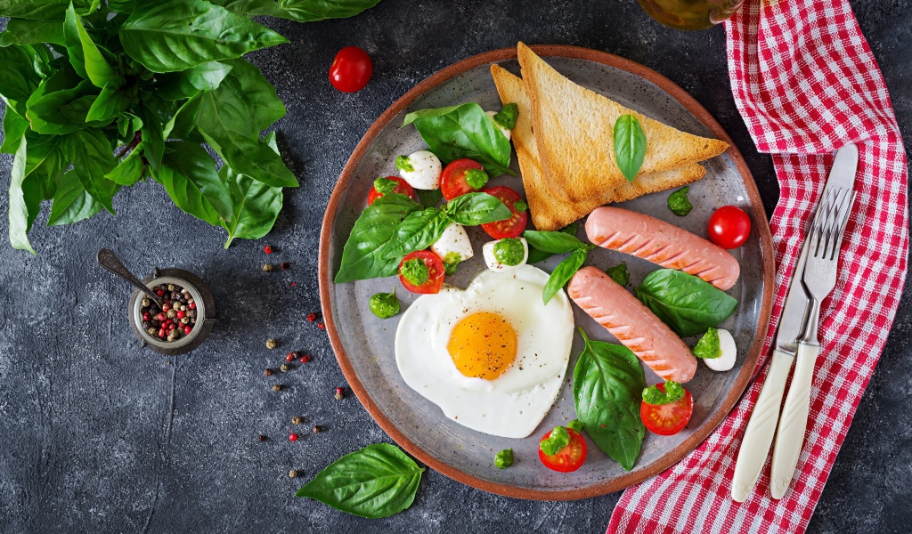 Яичница на тарелке с помидорами, гренками, сыром, сосисками и зеленью базилика