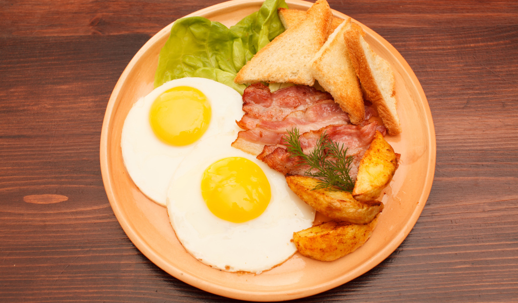 Яичница с беконом, картофелем фри и гренками на столе 