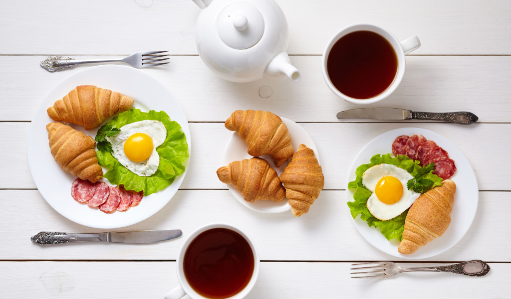 Яичница с колбасой и круассанами на столе чаем 