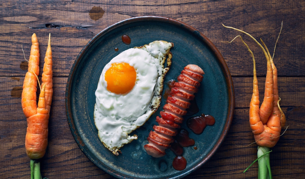 Яичница с сосиской на столе с морковью 