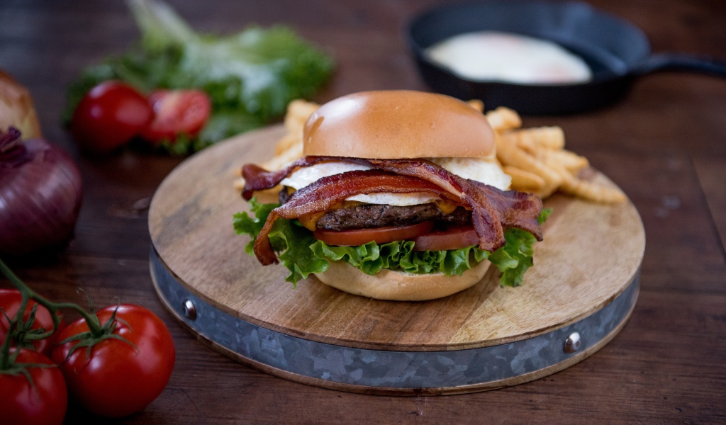 Гамбургер с беконом на столе с овощами