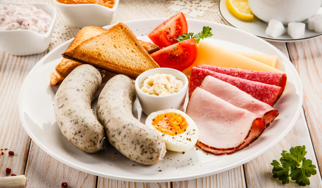 Большая белая тарелка с колбасой, яйцами, помидорами, тостами и сыром