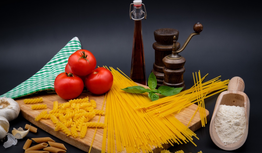 Макаронные изделия на столе с мукой, помидорами и специями