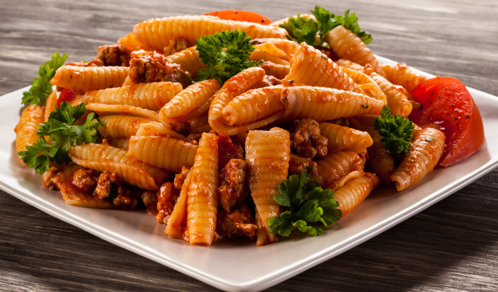 Паста с мясом, петрушкой и помидорами на белой тарелке