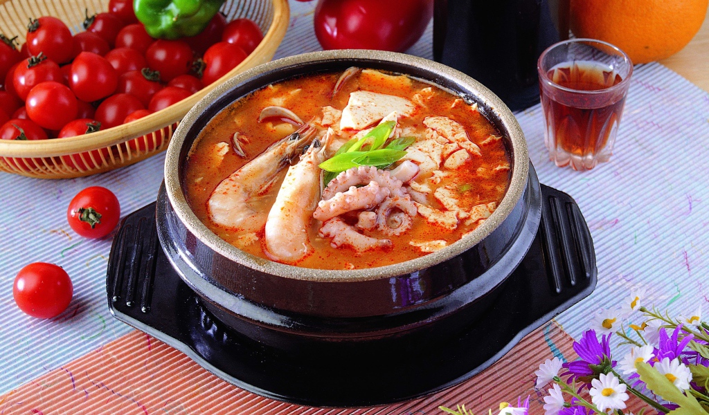 Тарелка красного супа с морепродуктами на столе с овощами 