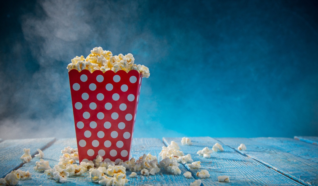 Попкорн в картонном пакете на голубом столе 