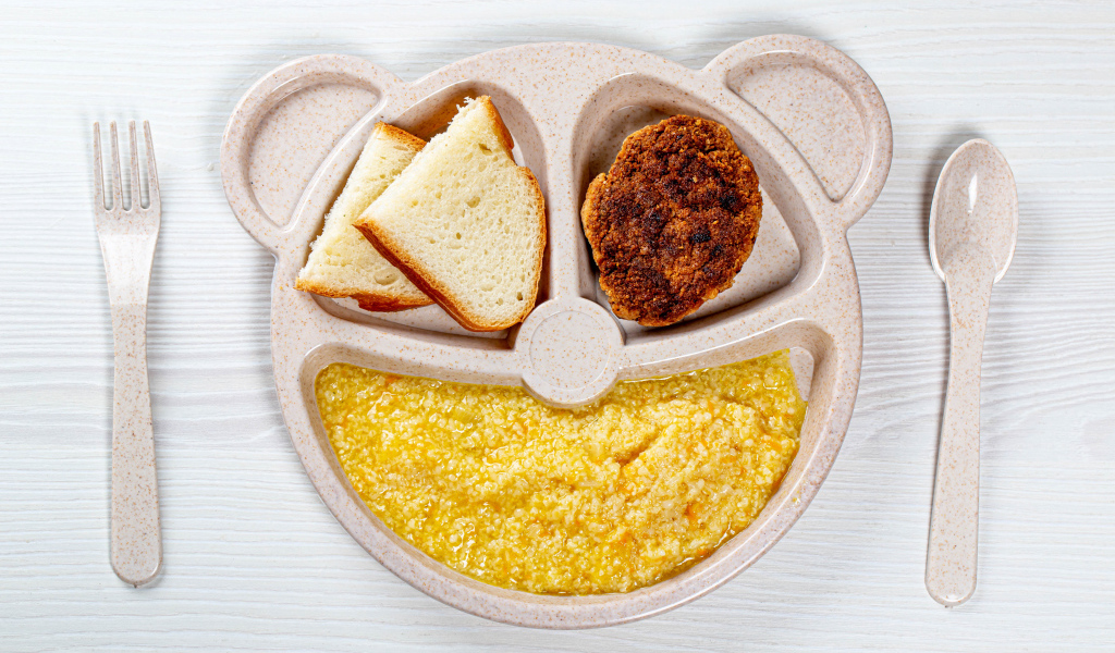 Каша на тарелке с котлетой и хлебом для ребенка