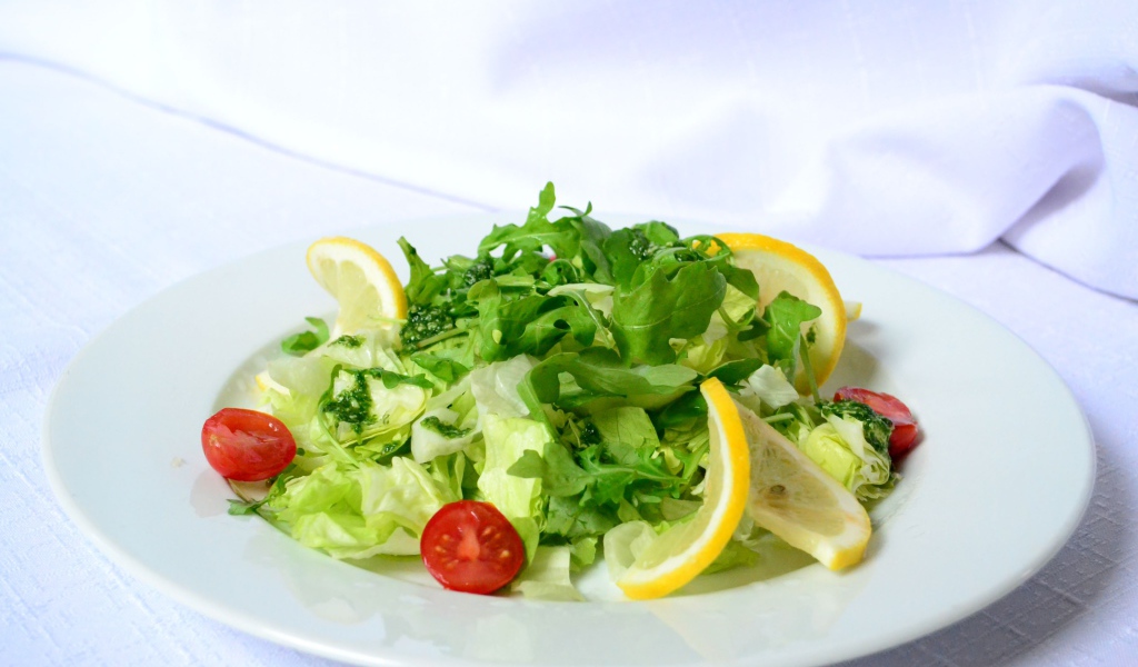 Салат с рукколой, лимоном и помидорами на белой тарелке
