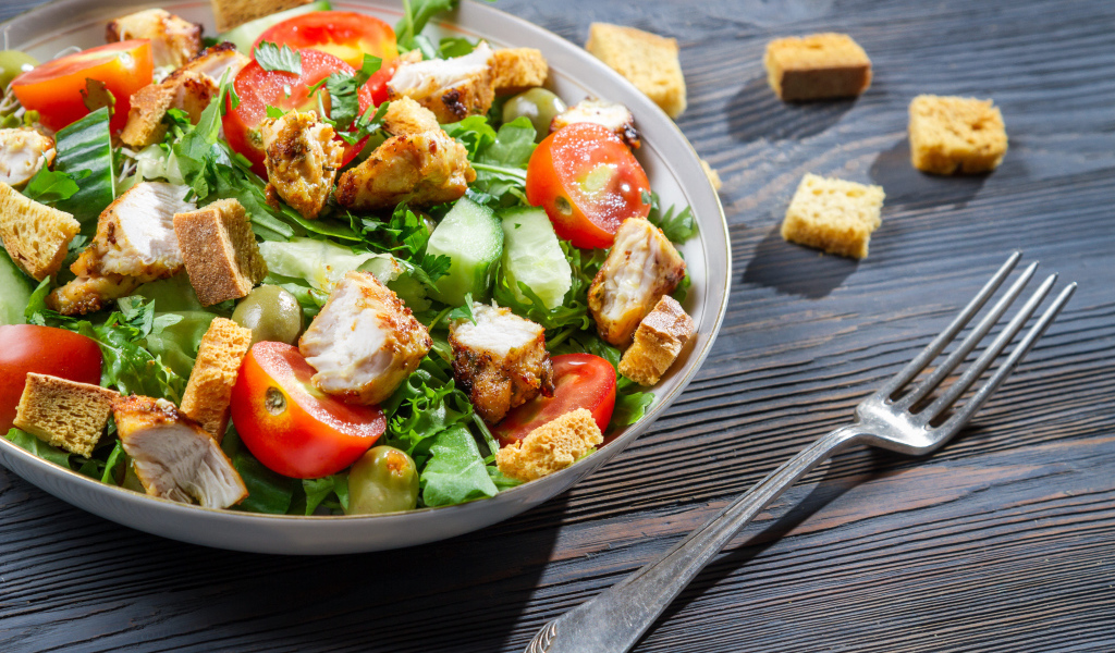 Салат с овощами, сухариками и курицей и на столе с вилкой