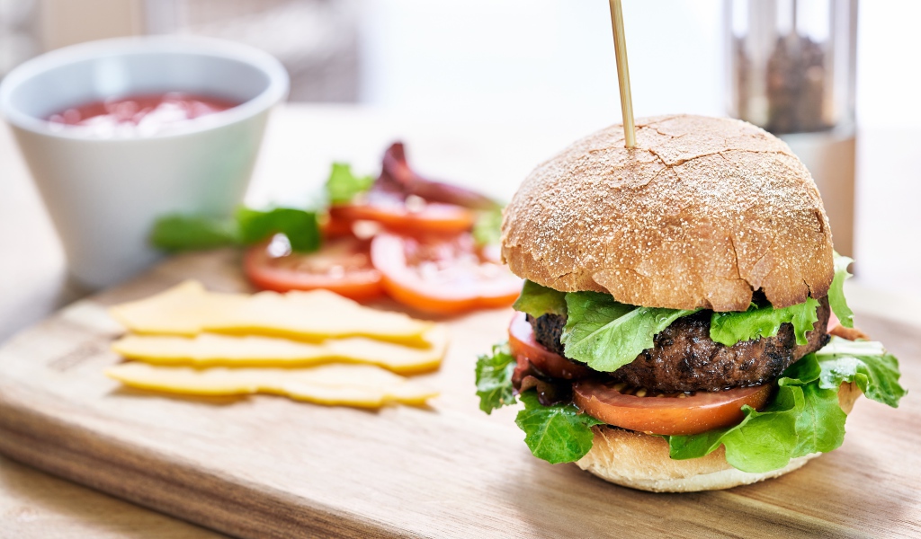 Аппетитный гамбургер на доске с сыром и помидорами