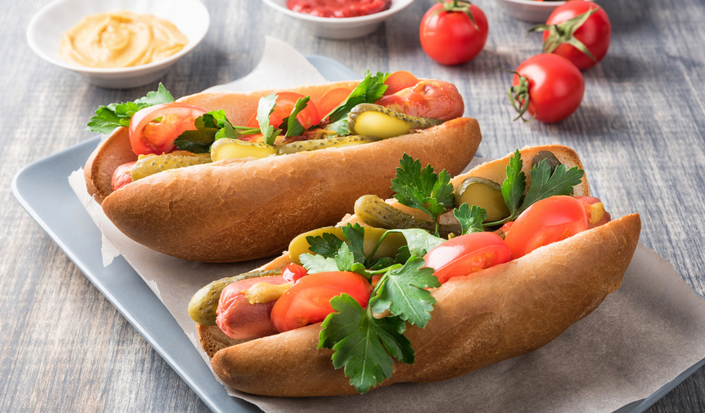 Two hotdogs with sausage, cucumbers and tomatoes