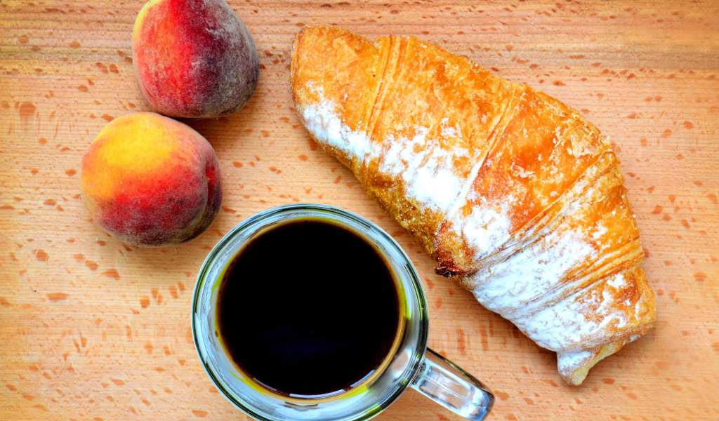 Два персика на столе с кофе и круассаном