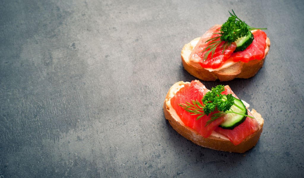 Два бутерброда с красной рыбой, огурцом и зеленью на черном фоне