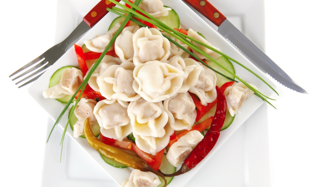 Белая тарелка с пельменями, красным перцем и огурцами