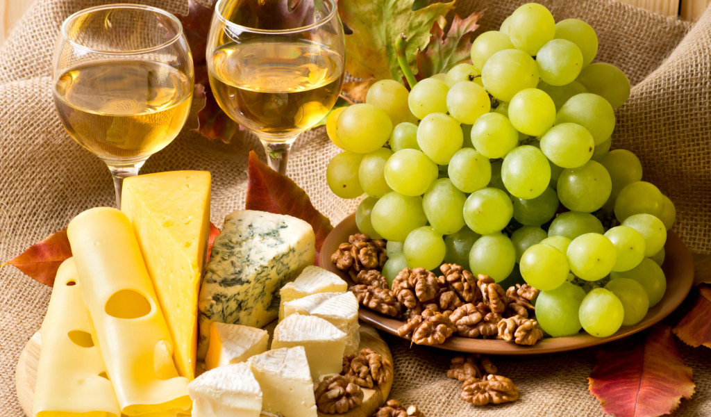 Белое вино на столе с сыром, виноградом и орехами