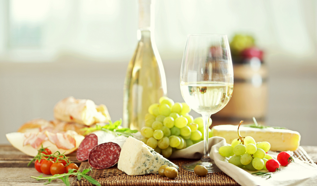 Белое вино на столе с сыром, колбасой и виноградом