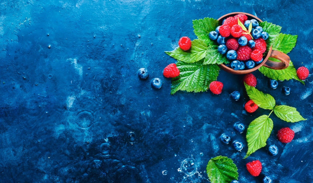 Чашка с ягодами черники и малины на синем столе