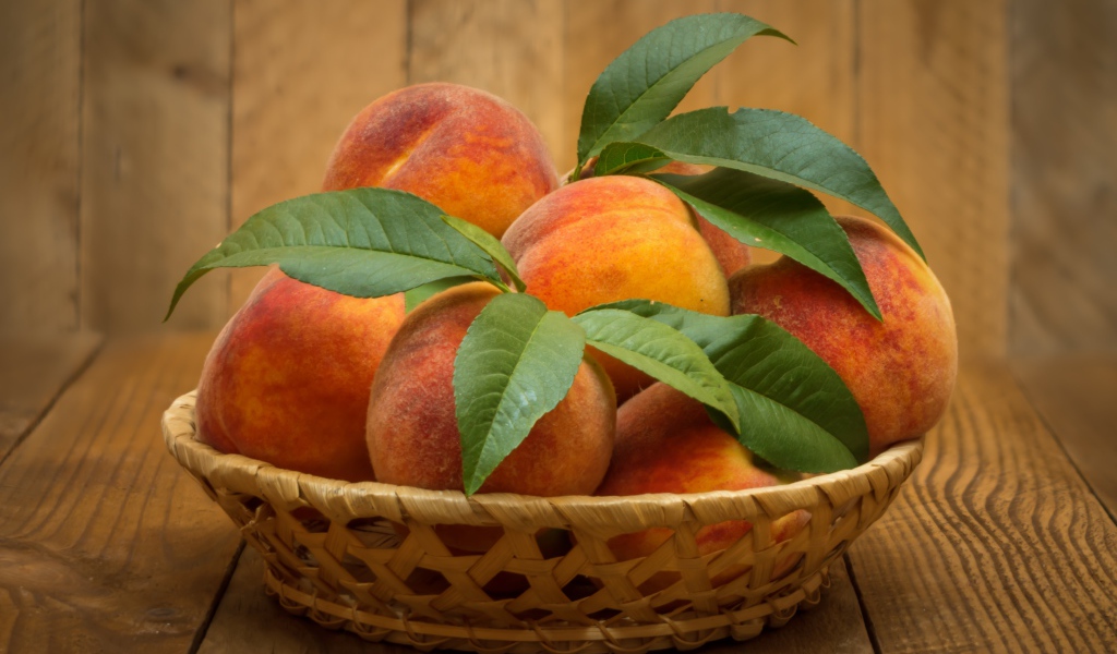 Корзинка персиков с зелеными листьями на столе