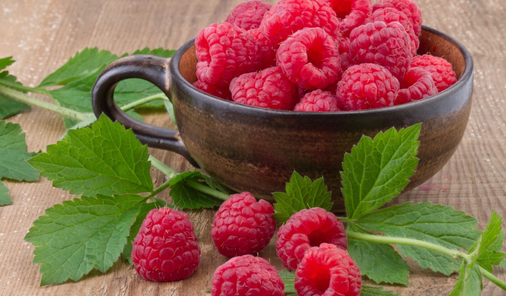 Чашка со свежей малиной на столе с зелеными листьями