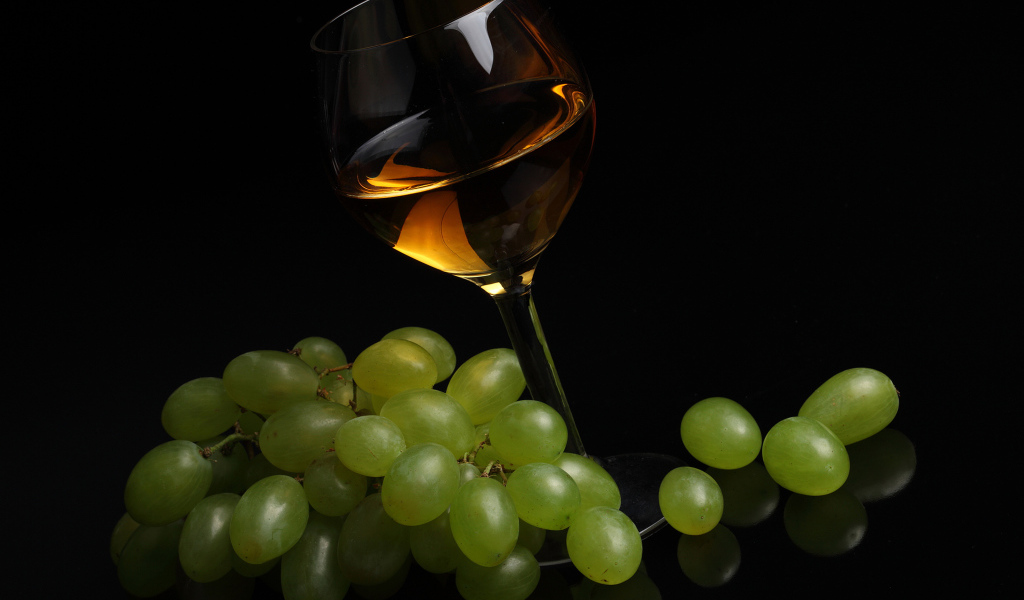Бокал вина с белым виноградом на черном фоне