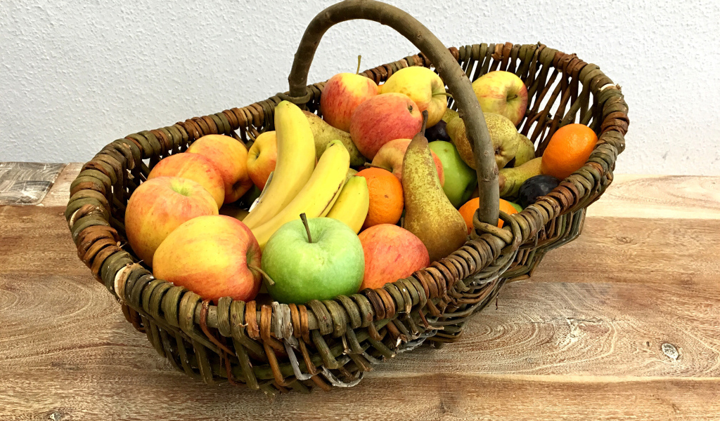 Спелые фрукты в плетеной корзине на столе