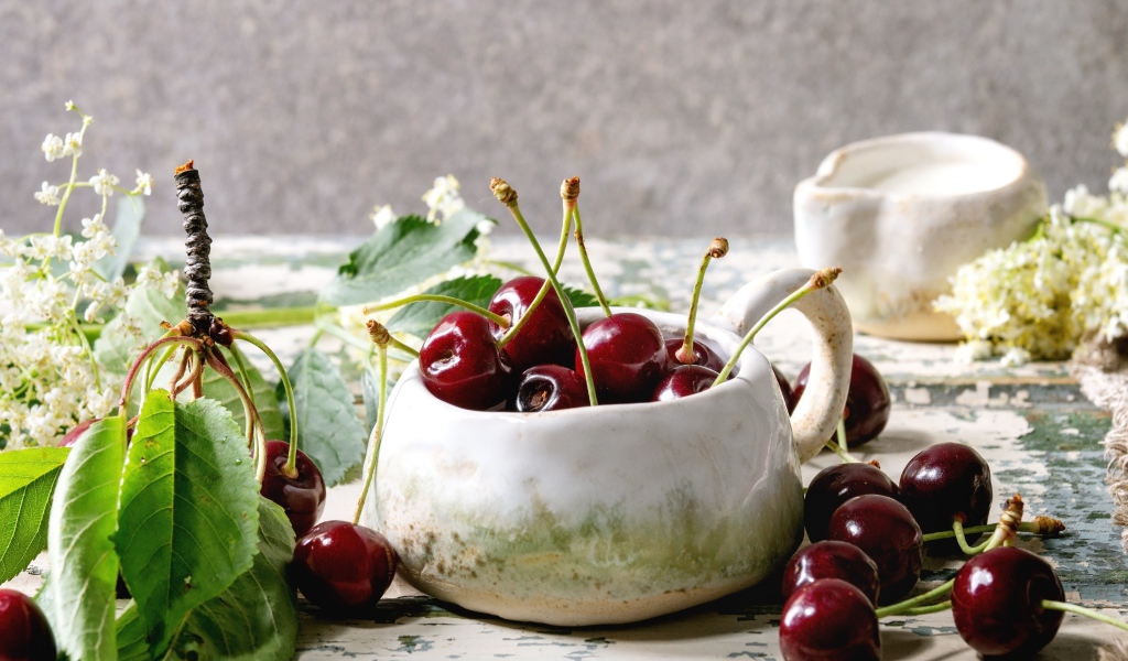 Спелые красные черешни на столе в белом чайнике