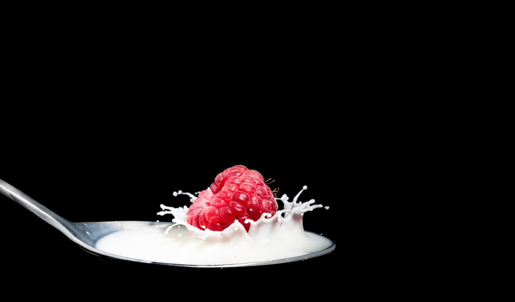 Спелая красная малина с ложке с молоком на черном фоне