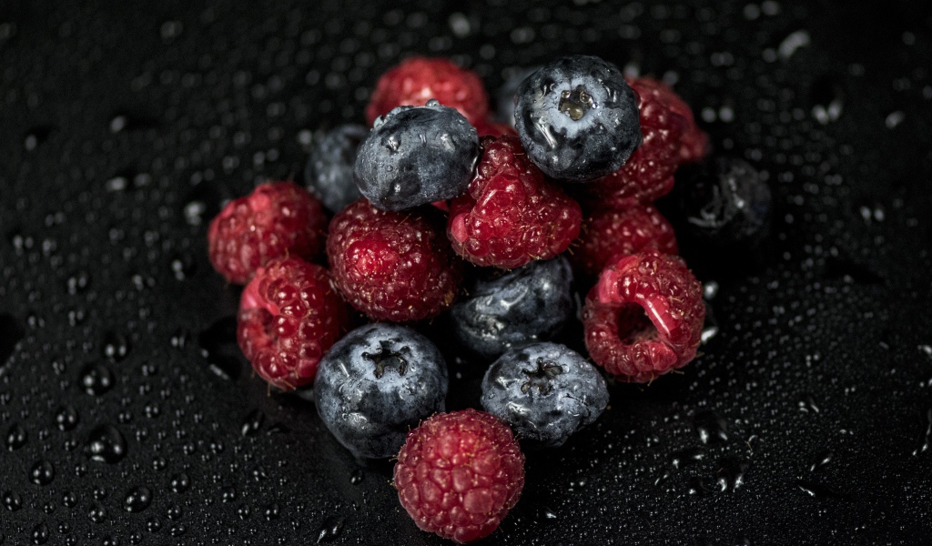Мокрые ягоды черники и малины на черном фоне