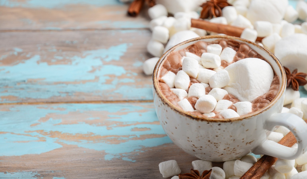 Чашка какао с маршмеллоу на столе с корицей и сладостями