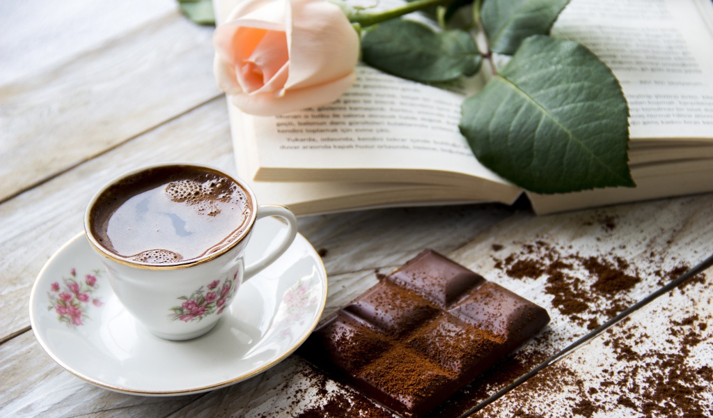 Чашка кофе на столе с шоколадом, книгой и розой