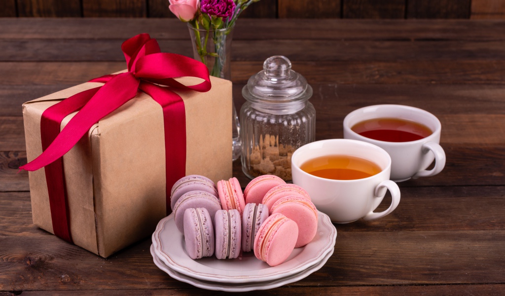 Подарок с красной лентой на столе с макарунами и чаем 