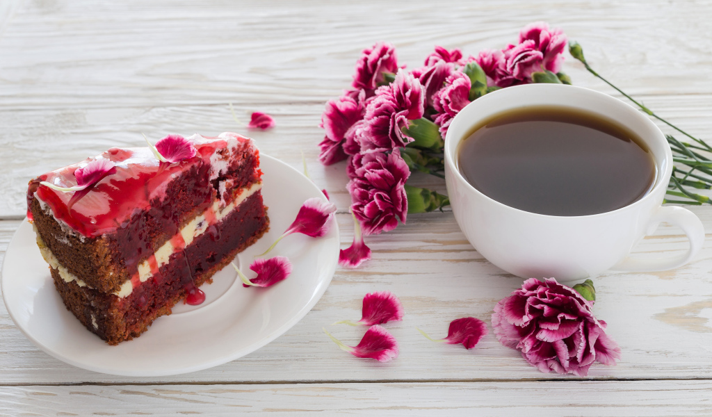 Кусок торта на столе с букетом гвоздик и чашкой кофе