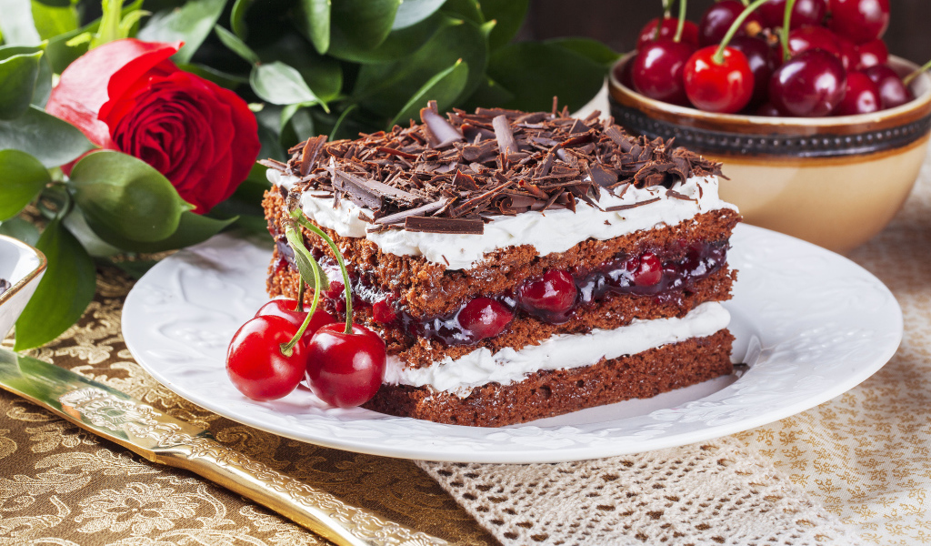 Кусок торта с вишней, шоколадной крошкой на столе с розой