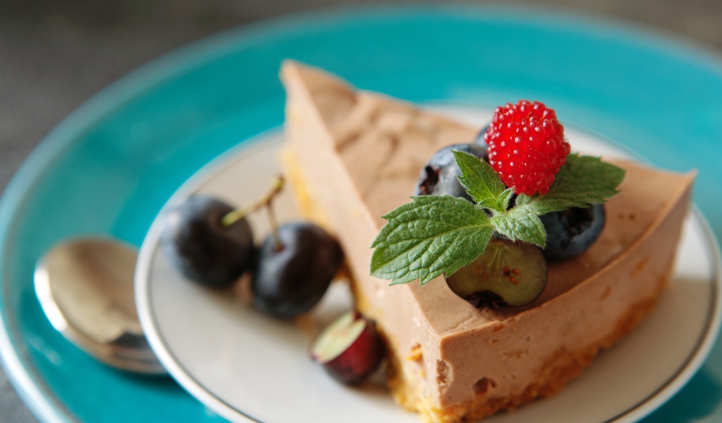 Кусок чизкейка на тарелке с ягодами черники и малиной
