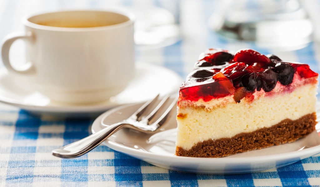 Кусок чизкейка с ягодами и желе на столе с чашкой кофе