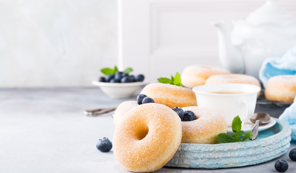 Аппетитные пончики с сахарной пудрой на столе с черникой