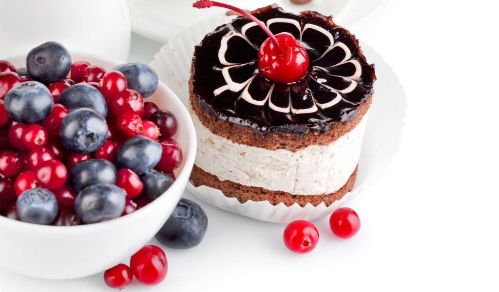 Пирожное с вишней на белом фоне с ягодами черники и клюквы