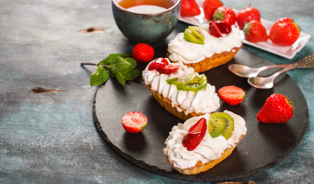 Пирожные с киви и клубникой на столе с чаем