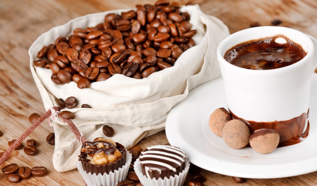 Шоколадные конфеты на столе с чашкой кофе и мешком с кофейными зернами
