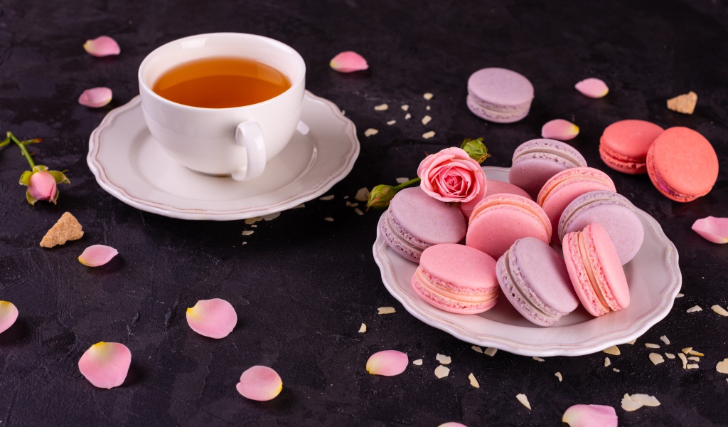 Нежный десерт макарон на столе с чашкой чая и розой