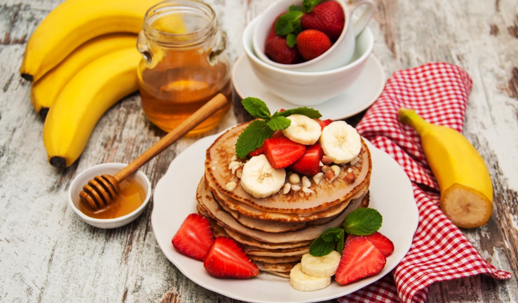 Оладьи с бананами и клубникой на столе с медом