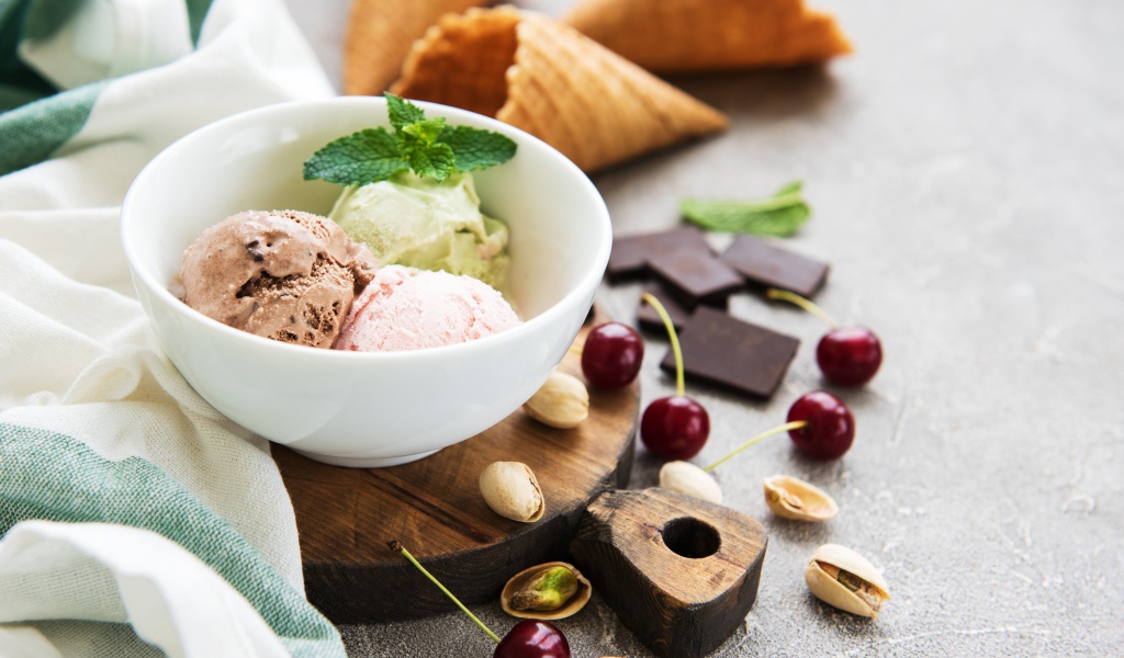 Шарики мороженого на столе вафельными рожками, черешней и фисташками