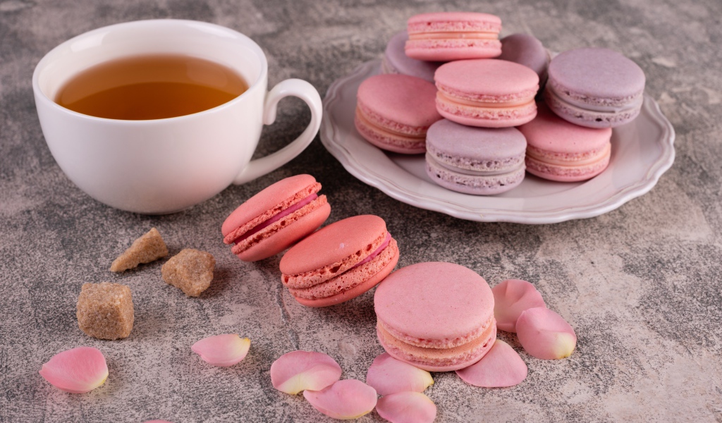 Сладкий десерт макарун на столе с чашкой чая, сахаром и лепестками розы