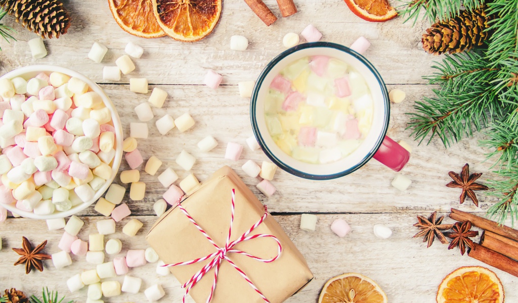 Кружка горячего напитка на столе с маршмеллоу, пряностями и подарком