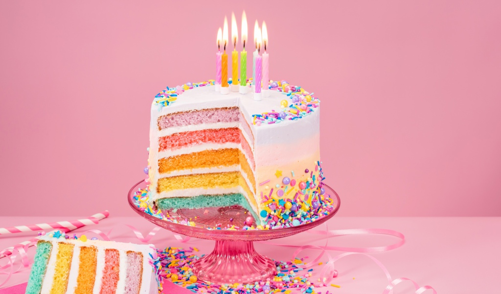 Разноцветный праздничный торт со свечами на розовом фоне