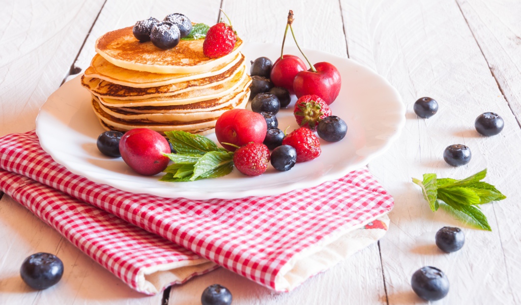 Оладья на белой тарелке с ягодами черники, черешни и клубники