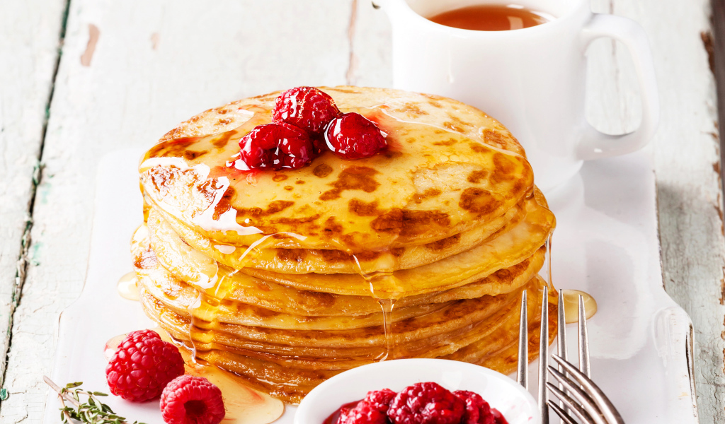 Панкейки с медом и ягодами малины на столе с чаем