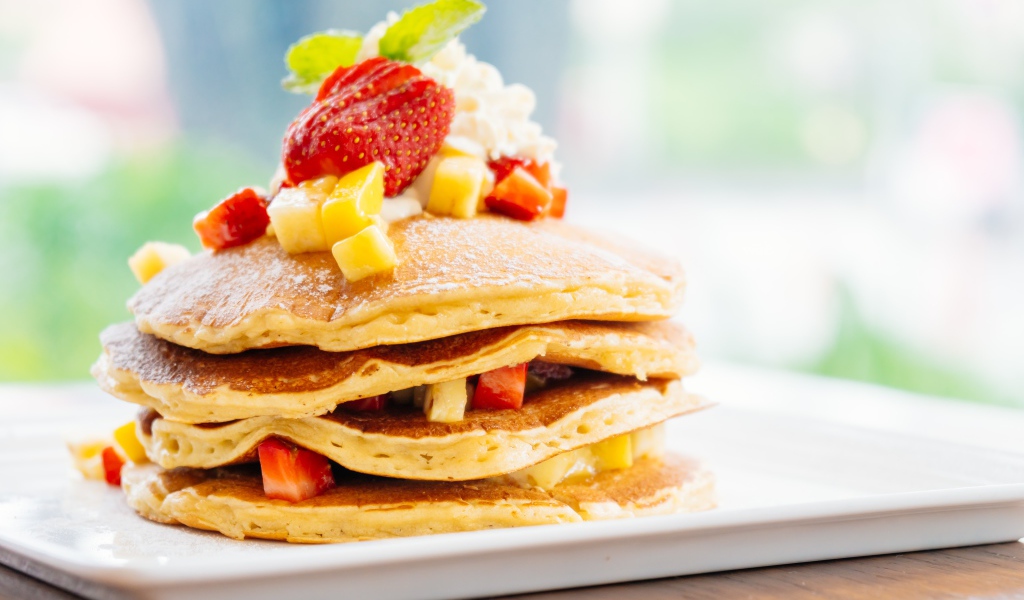 Оладьи с сахарной пудрой, сливками и кусочками клубники и ананаса